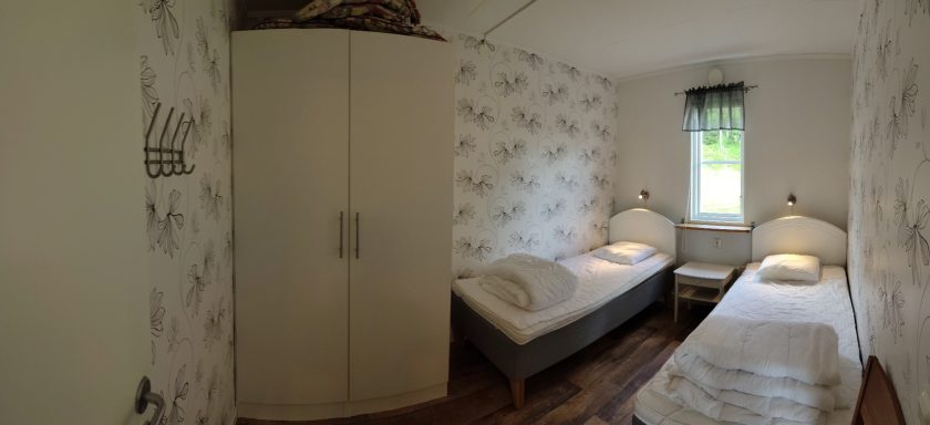 Sovrum med två sängar, garderob och blommigt tapetserat väggar.