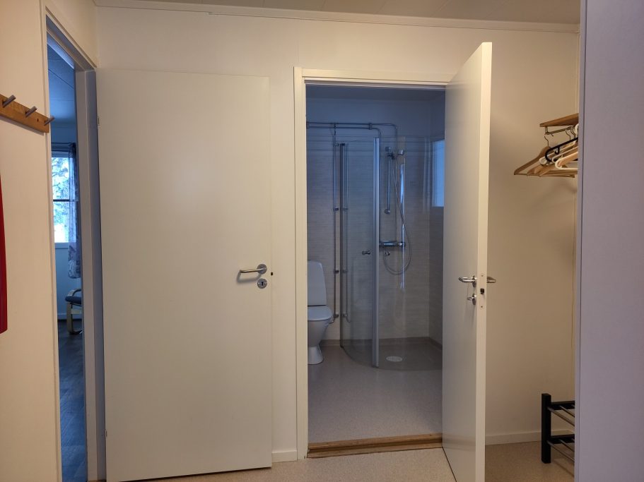 Hall Två öppna dörrar som leder till ett badrum med dusch och toalett.