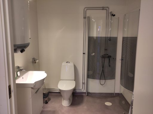 Badrum med toalett, handfat och dusch i en neutral färgsättning.